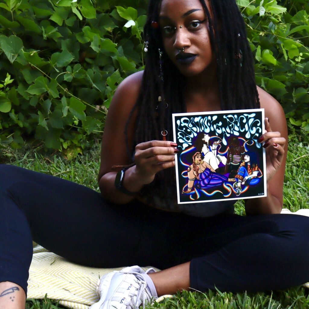 Ayeola sits on the grass, holding an illustration and looking at the camera