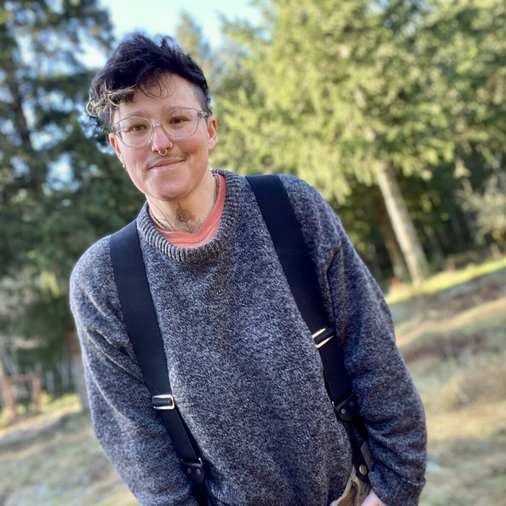 Bird wears a large sweater and suspenders, with woods in the background