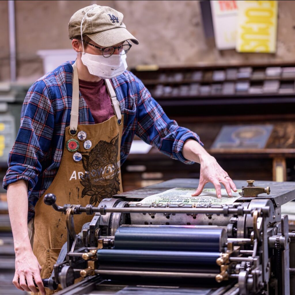 Etai printing on a Vandercook proof press, with type cases in the background